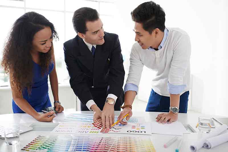 Klassische Kommunikation - Corporate Design Marketingmitarbeiter definieren die Farben für eine Broschüre mit einem Pantone Farbfächer