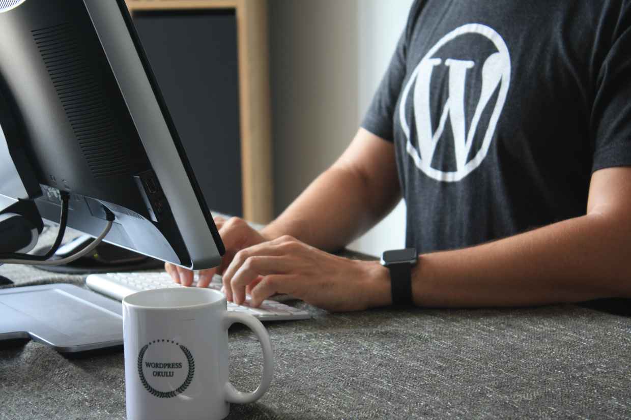 Person mit schwarzem T-Shirt und WordPress Logo vor Computer